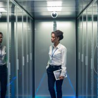 African American woman with tablet while walking in corridor of data center and checking hardware on server racks